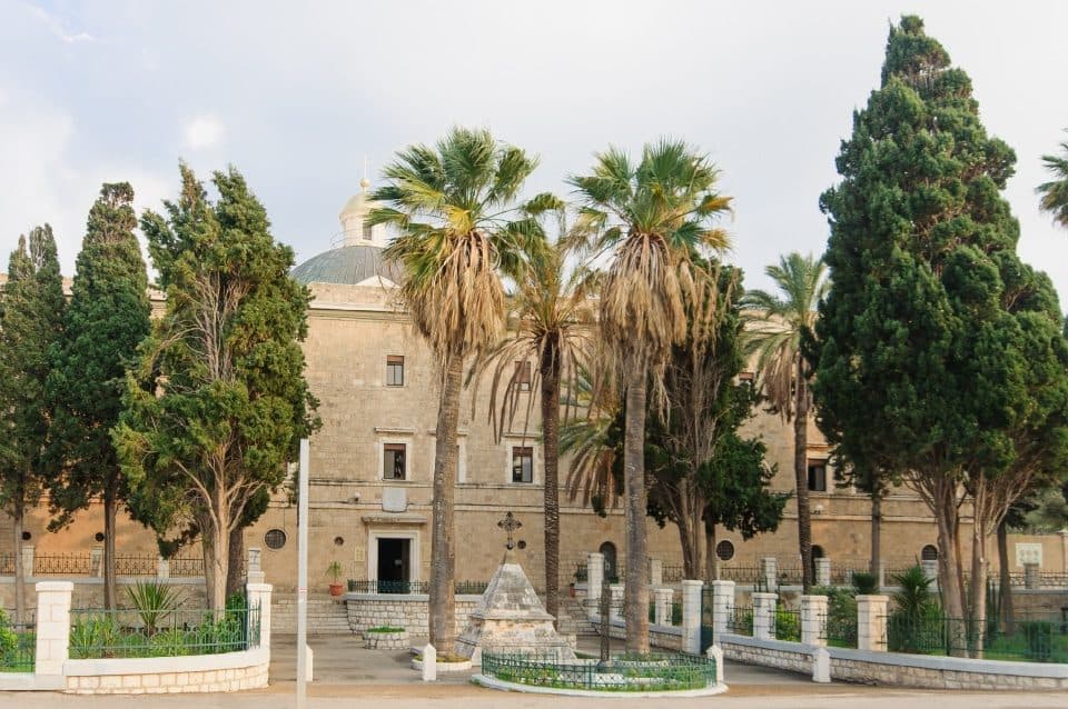 חזית מנזר סטלה מאריס בחיפה, מוקפת עצי ברוש ודקלים